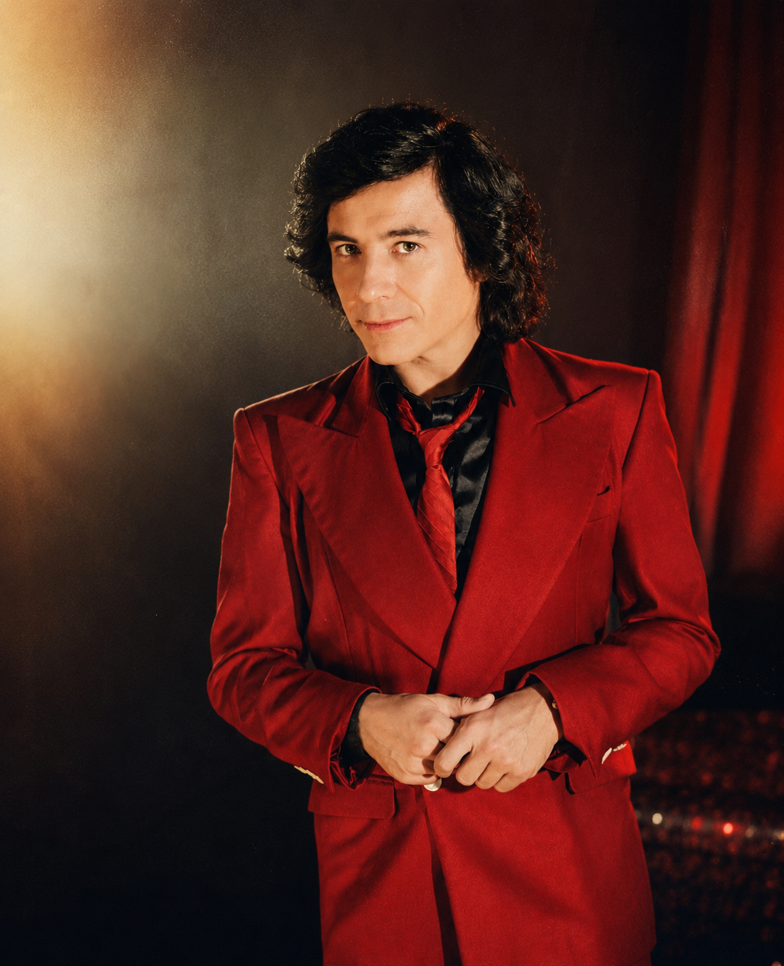 Retrato de Marcelo Jiménez con traje rojo junto a una cortina de teatro